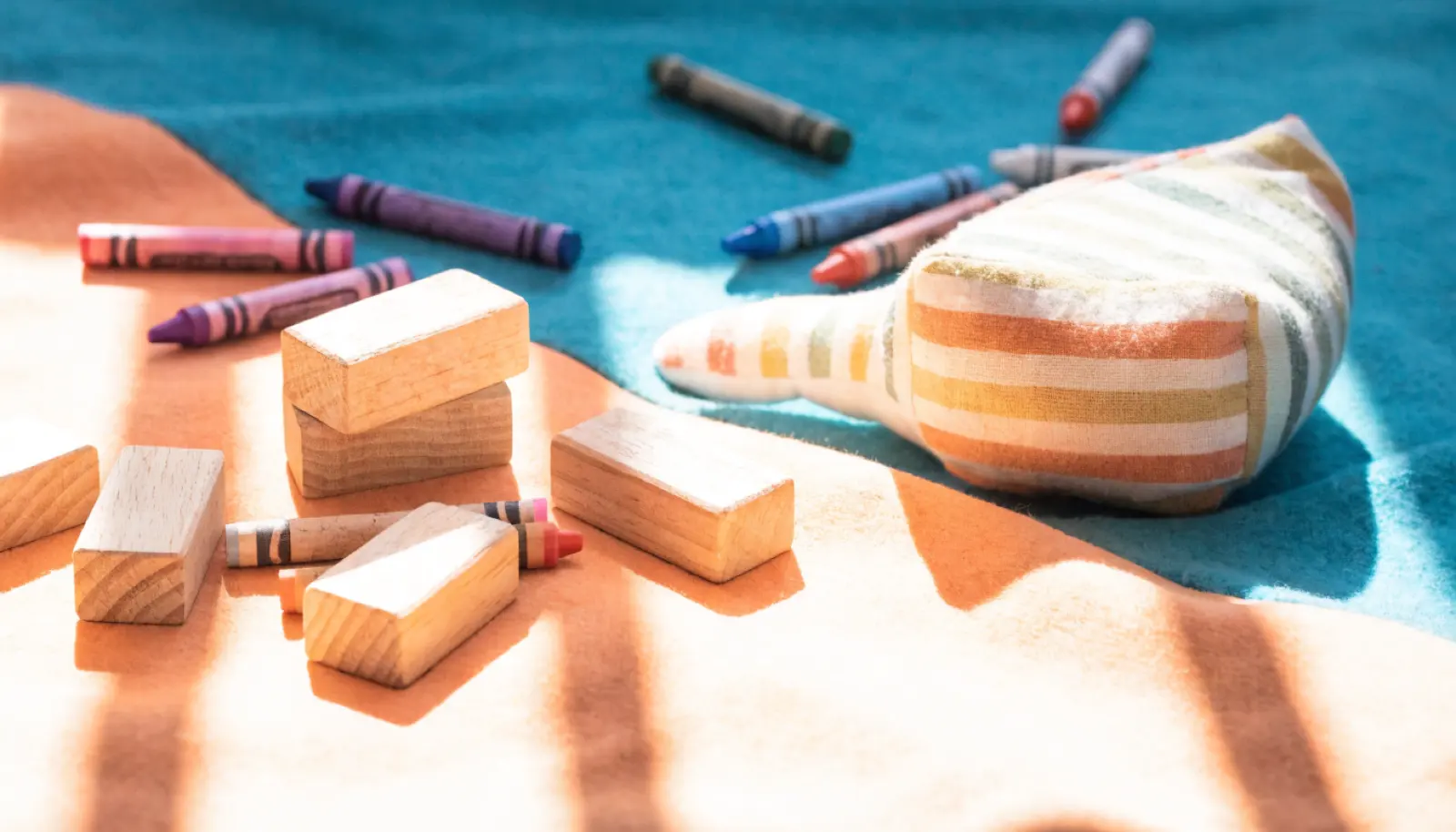 Battaniyenin üzerine dağılmış pastel boya kalemleri, ahşap bloklar ve bez bir oyuncak